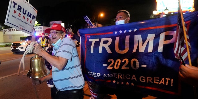 Rafael Fagundo rings a bell as he and other supporters of President Donald Trump chant and wave flags outside the Versailles Cuban restaurant during a celebration on election night, Tuesday, Nov. 3, 2020, in the Little Havana neighborhood of Miami. (AP Photo/Wilfredo Lee)