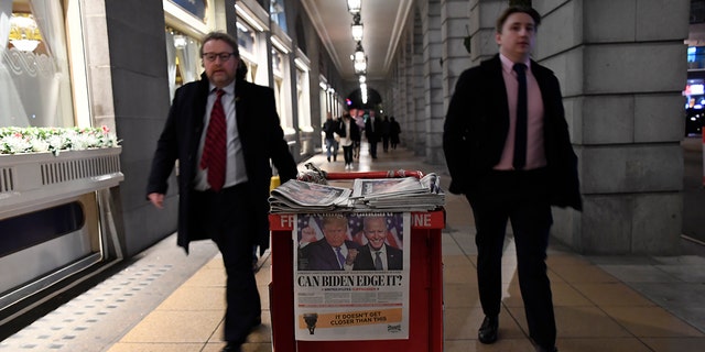 People walk past a pile of Evening Standard newspapers displaying a picture of US presidential candidates President Donald Trump and Joe Biden, in London, Wednesday, Nov. 4, 2020. (AP Photo/Alberto Pezzali)