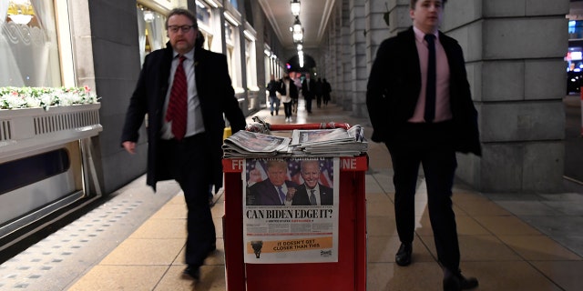 People walk past a pile of Evening Standard newspapers displaying a picture of US presidential candidates President Donald Trump and Joe Biden, in London, Wednesday, Nov. 4, 2020. (AP Photo/Alberto Pezzali)