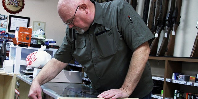 John Erickson points to half-empty handgun racks in his Bridgeport., Neb., shop earlier this month. A recent Gallup poll showed a decline in support for tougher gun laws. Gun shops, big box or locally owned stores said they're struggling to keep popular firearms and ammunition stocked because of supply shortages and increased demand. (Danielle Prokop/The Star-Herald via AP)