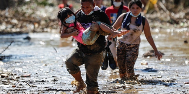 A man carries a girl through debris and floods in the typhoon-damaged Kasiglahan village in Rodriguez, Rizal province, Philippines on Friday, Nov. 13, 2020. Thick mud and debris coated many villages around the Philippine capital Friday after Typhoon Vamco caused extensive flooding that sent residents fleeing to their roofs and killing dozens of people. (AP Photo/Aaron Favila)