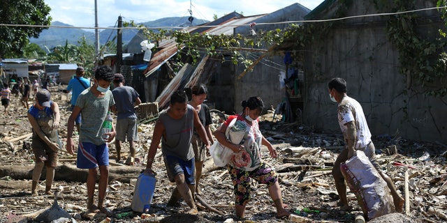 Residents walk through mud and debris at the typhoon-damaged Kasiglahan village in Rodriguez, Rizal province, Philippines on Friday, Nov. 13, 2020. Thick mud and debris coated many villages around the Philippine capital Friday after Typhoon Vamco caused extensive flooding that sent residents fleeing to their roofs and killing dozens of people. (AP Photo/Aaron Favila)