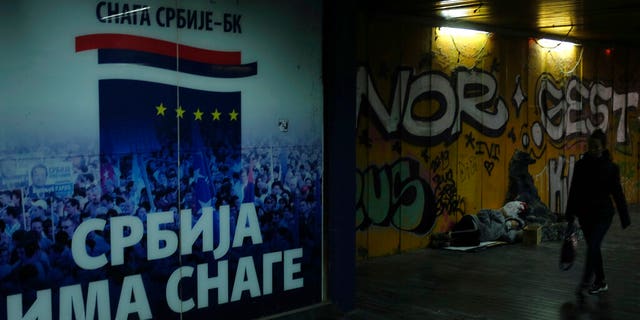 A woman walks through an underground passage by a homeless person and inscription on the wall reading "Serbia has the strength" in Belgrade, Serbia, Monday, Nov. 16, 2020. 