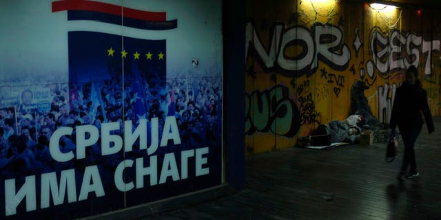 A woman walks through an underground passage by a homeless person and inscription on the wall reading "Serbia has the strength" in Belgrade, Serbia, Monday, Nov. 16, 2020.