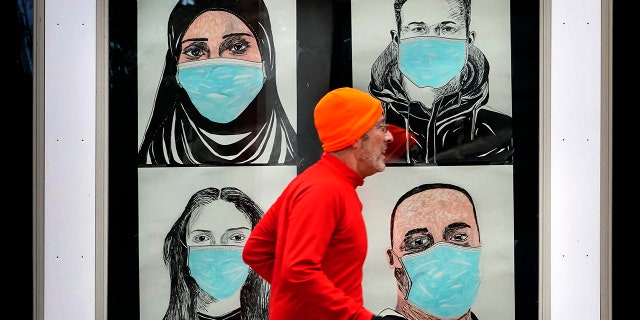 In this Nov. 16, 2020, file photo, a runner passes by a window displaying portraits of people wearing face coverings to help prevent the spread of the coronavirus in Lewiston, Maine. (AP Photo/Robert F. Bukaty, File)