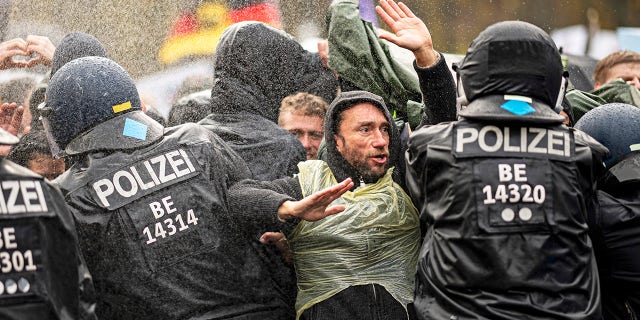 Police officers try to push back protesters on a blocked road between the Brandenburg Gate and the Reichstag building, home of the German federal parliament, as people attend a protest rally in front of the Brandenburg Gate in Berlin, Germany, Wednesday, Nov. 18, 2020 against the coronavirus restrictions in Germany. (Fabian Sommer/dpa via AP)