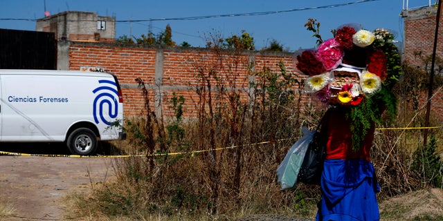A woman carrying flowers walks past a forensic truck where technicians are searching for bodies in El Salto, outside the metropolitan area of Guadalajara, Jalisco state, Monday, Nov. 23, 2020. Mexican authorities have recovered 113 bodies and additional human remains from the site. (AP Photo/Refugio Ruiz)