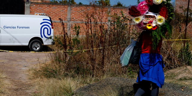 A woman carrying flowers walks past a forensic truck where technicians are searching for bodies in El Salto, outside the metropolitan area of Guadalajara, Jalisco state, 월요일, 11 월. 23, 2020. Mexican authorities have recovered 113 bodies and additional human remains from the site. (AP Photo/Refugio Ruiz)