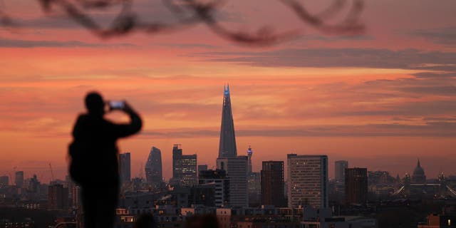 A person takes a photo of the skyline with the Shard building in the center, at sunset, from Greenwich Park in London, Tuesday, Nov. 24, 2020. (Yui Mok/PA via AP)