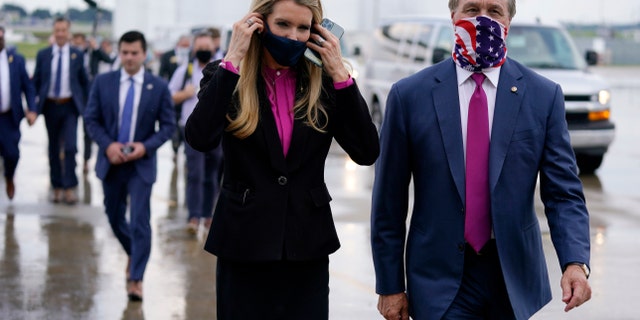 In this July 15, 2020, file photo Sen. Kelly Loeffler, R-Ga., puts on a face mask as she walks with Sen. David Perdue, R-Ga., right, at UPS Hapeville Airport Hub in Atlanta. (AP Photo/Evan Vucci, File)