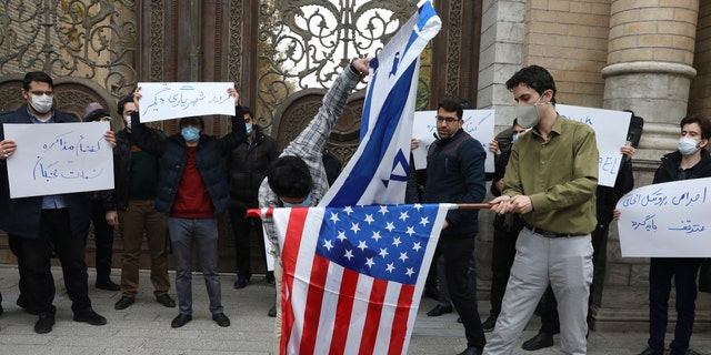 Two protesters burn the representation of the U.S. and Israeli flags as the others hold placards condemning inspections by the UN nuclear agency (IAEA) on Iran's nuclear activities and the country's nuclear talks with world powers during a gathering in front of Iranian Foreign Ministry on Saturday, Nov. 28, 2020 in Tehran. Supreme Leader Ayatollah Ali Khamenei is calling for “definitive punishment” of those behind killing of Mohsen Fakhrizadeh, the scientist linked to Tehran’s disbanded military nuclear program. (AP Photo/Vahid Salemi)