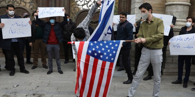 Two protesters burn the representation of the U.S. and Israeli flags as the others hold placards condemning inspections by the UN nuclear agency (IAEA) on Iran's nuclear activities and the country's nuclear talks with world powers during a gathering in front of the Iranian Foreign Ministry on Saturday, Nov. 28, 2020, in Tehran. (AP Photo/Vahid Salemi)