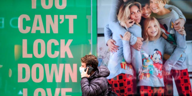 A man walks past a poster in the window of a clothing shop in Manchester, England, Saturday Nov. 28, 2020.