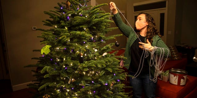 Ani Sirois puts lights and decorations on the family's Christmas tree at her home on Tuesday, Nov. 24, 2020 in Portland, Ore. (AP Photo/Paula Bronstein)