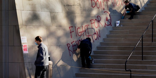 A man walks past police collecting evidence after graffiti was found outside a polling place at the National World War I museum Tuesday, Nov. 3, 2020, in Kansas City, Mo.