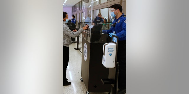 A Transportation Security Administration (TSA) agent wearing a protective face mask and shield checks the identification of a travelers Photographer: George Frey/Bloomberg via Getty Images