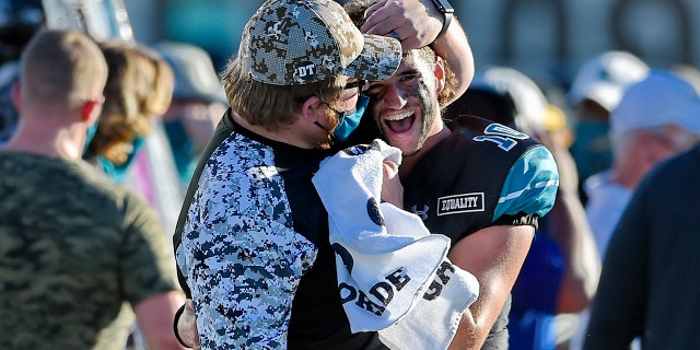 Coastal Carolina quarterback Grayson McCall (10) is hugged by a member of the coaching staff during the second half of an NCAA college football game against Appalachian State, Sabato, Nov. 21, 2020, in Conway, S.C. Coastal Carolina won 34-23. (AP Photo/Richard Shiro)
