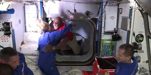 In this frame grab from NASA TV, astronaut Victor Glover, center, is greeted by astronaut Kate Rubins as he enters the International Space Station from the vestibule between the SpaceX Dragon capsule and the ISS, early Tuesday, Nov. 17, 2020. At right is Expedition 64 commander Sergey Ryzhikov. (NASA TV via AP)