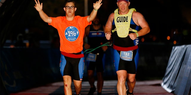   Chris Nikic and guide Dan Grieb cross the IRONMAN Florida finish line on November 7 in Panama City Beach, Florida.  Chris Nikic became the first Ironman finisher with Down syndrome.  (Photo by Michael Reaves / Getty Images for IRONMAN)