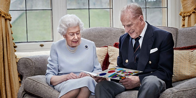 In this image released on Thursday, November 19, 2020, British Queen Elizabeth II and Prince Philip, Duke of Edinburgh look at a homemade wedding anniversary card, given to them by their great-grandchildren, the Prince George, Princess Charlotte and Prince Louis, as the royal couple sit in the Oak Room at Windsor Castle, England on November 17, 2020, ahead of their 73rd wedding anniversary.  (Chris Jackson / Pool via AP)