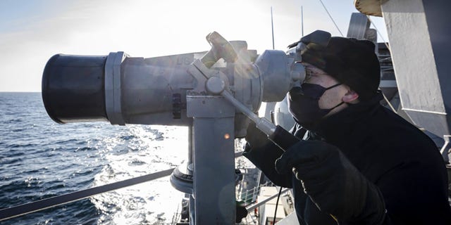 Ensign James Bateman, of Huntsville, Alabama, scans the horizon using `` big eyes '' while keeping watch on the deck wing of the guided missile destroyer USS John S. McCain on Tuesday.