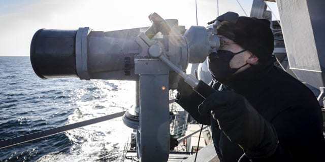 Ensign James Bateman, of Huntsville, Alabama, scans the horizon using `` big eyes '' while keeping watch on the deck wing of the guided missile destroyer USS John S. McCain on Tuesday.