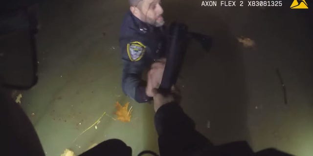 An officer holds onto another officer in the chilly river water while working to help the trapped woman.