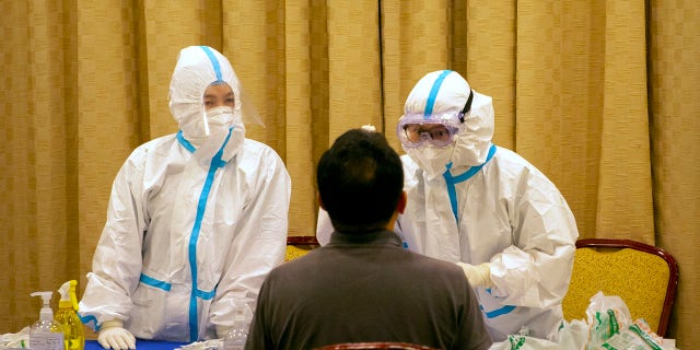 Workers in protective suits administer a COVID-19 test in Wenchang in southern China's Hainan Province on Sunday. (AP Photo/Mark Schiefelbein)