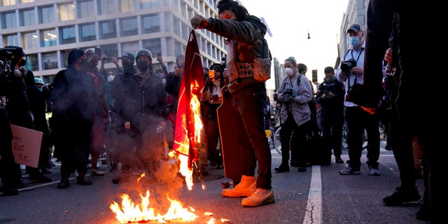 A counter-protester burns a Trump 2020 flag after supporters of President Trump held pro-Trump marches Saturday, Nov. 14, 2020, in Washington. (AP Photo/Jacquelyn Martin)