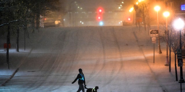 A dog walker crosses a street during Tuesday night's snow storm in downtown Minneapolis, Nov. 10, 2020. (Aaron Lavinsky/Star Tribune via AP)