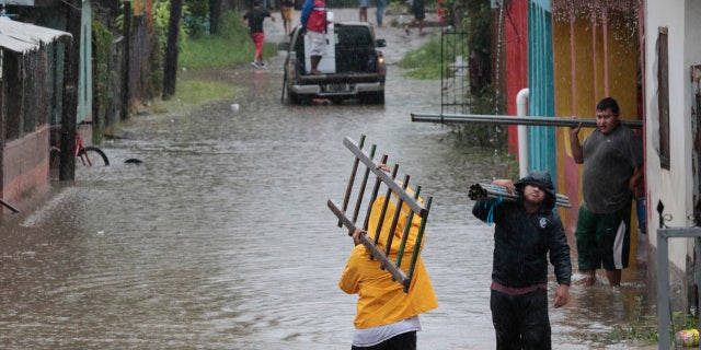 A man walks through a flooded road with a ladder in San Manuel, Honduras, Wednesday, Nov. 4, 2020.
