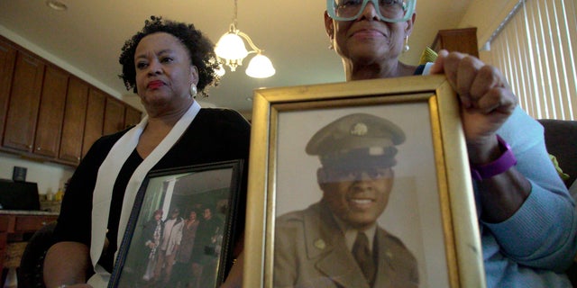 Sisters Barbara Leak-Watkins, right, and Alberta Lynn Fantroy pose with photos of their late father, Alex Leak Jr., an Army veteran who died in July after collapsing from dehydration at his assisted-living facility.