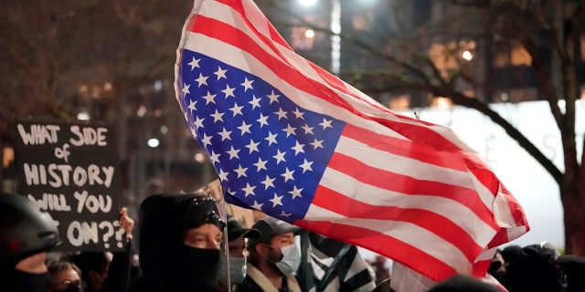 A person carries an upside-down flag as people march on the night of the election in Seattle, Tuesday, Nov. 3, 2020.