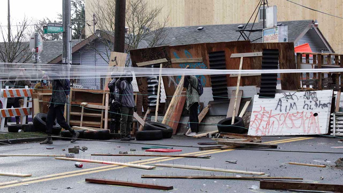 Protesters stand behind barricades at their encampment outside a home in Portland, Ore., on Wednesday, Dec. 9, 2020. Makeshift barricades erected by protesters are still up in Oregon's largest city a day after Portland police arrested about a dozen people in a clash over gentrification and the eviction of a family from a home. (AP Photo/Gillian Flaccus)