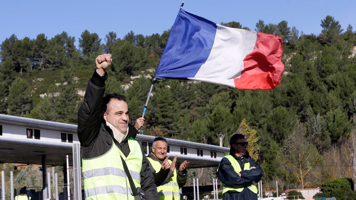 A demonstrators wearing a yellow vest clenches his fist as protesters open the toll gates on a motorway near Aix-en-Provence, southeastern France, Tuesday, Dec. 4, 2018. French Prime Minister Edouard Philippe announced a suspension of fuel tax hikes Tuesday, a major U-turn in an effort to appease a protest movement that has radicalized and plunged Paris into chaos last weekend. (AP Photo/Claude Paris)