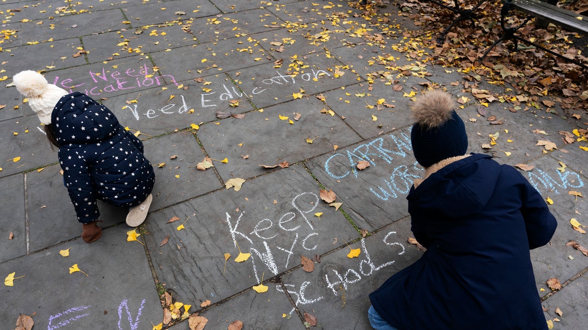 Students chalk graffiti on a sidewalk in front of New York's City Hall during a protest by parents and students opposing the closing of schools, Thursday, Nov. 19, 2020. (AP Photo/Mark Lennihan)