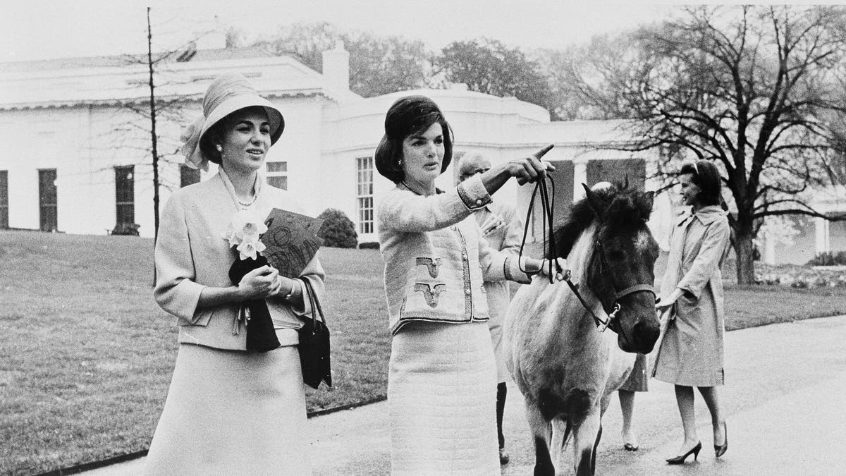 In this April 12, 1962, file photo first lady Jacqueline Kennedy gives a guided tour of the White House grounds to Empress Farah Pahlavi of Iran in Washington. Kennedy leads her daughter Caroline's pony, Macaroni, which had been nuzzling the empress, attracted by the daffodils she was carrying. (AP Photo/Pool)