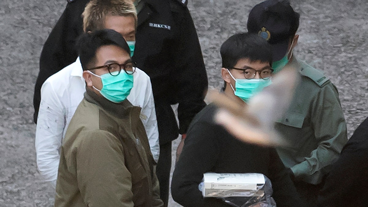 A bird flies as Hong Kong activists Joshua Wong, right, and Ivan Lam, left, are escorted by Correctional Services officers to get on a prison van before appearing in a court, in Hong Kong, Wednesday, Dec. 2, 2020. (AP Photo/Kin Cheung)