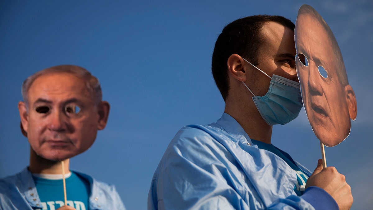 Israeli demonstrators hold masks depicting Israeli Prime Minister Benjamin Netanyahu, left, and Israeli Defense Minister Benny Gantz, right, during a protest against a parliamentary vote to dissolve the Knesset and send the country to its fourth elections in two years while it still hasn't approved a national budget for 2020, in Tel Aviv, Wednesday, Dec. 2, 2020. (AP Photo/Oded Balilty)