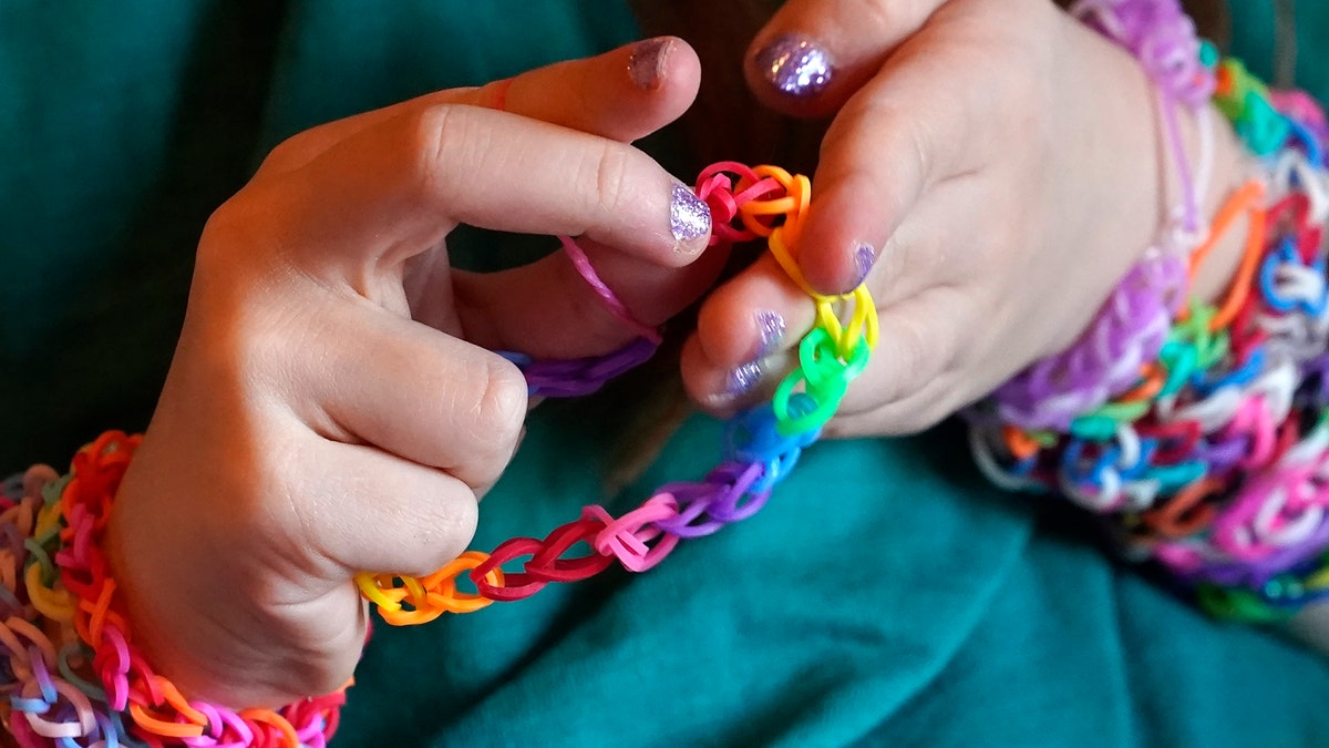 Hayley Orlinsky examines a bracelet she made from colorful rubber bands Wednesday, Dec. 2, 2020, in the bedroom of her Chicago home. The 7-year-old has spent most of the coronavirus pandemic crafting the bracelets as a fundraiser, earning nearly $20,000, to buy personal protective equipment for the Ann and Robert H. Lurie Children's Hospital. (AP Photo/Charles Rex Arbogast)