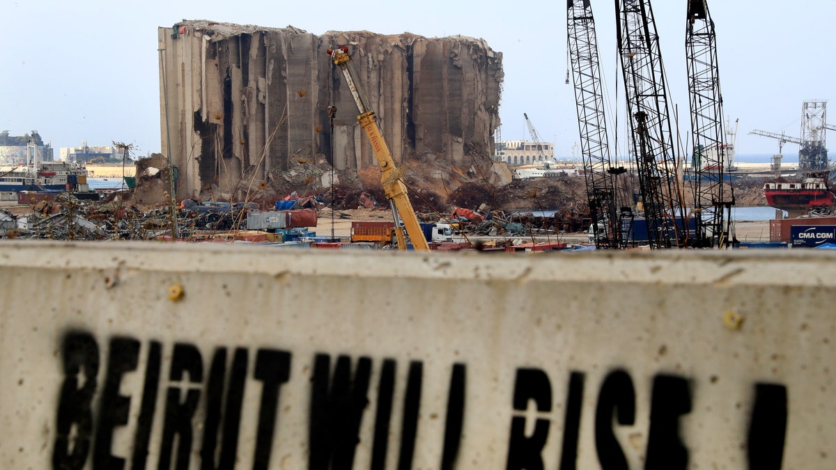 A slogan is painted on a barrier in front of towering grain silos gutted in the massive August explosion at the Beirut port that claimed the lives of more than 200 people, in Beirut, Lebanon, Wednesday, Dec. 2, 2020. (AP Photo/Hussein Malla)