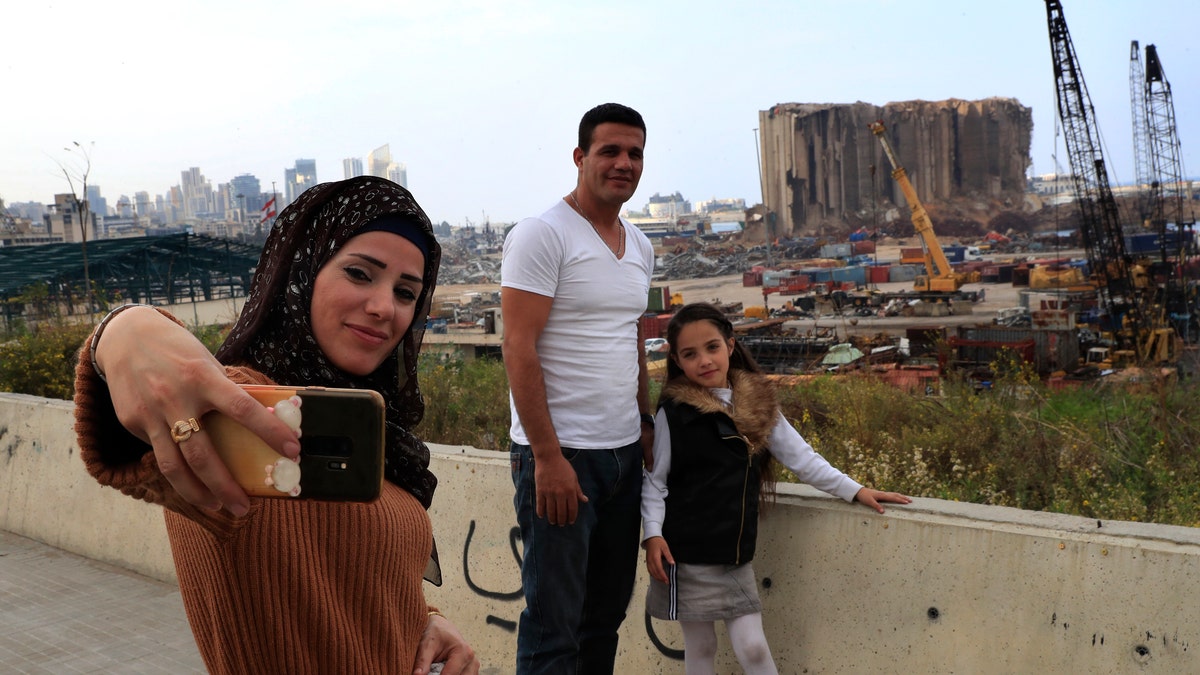 A Lebanese family takes a selfie in front of towering grain silos gutted in the massive August explosion at the Beirut port that claimed the lives of more than 200 people, in Beirut, Lebanon, Wednesday, Dec. 2, 2020. (AP Photo/Hussein Malla)