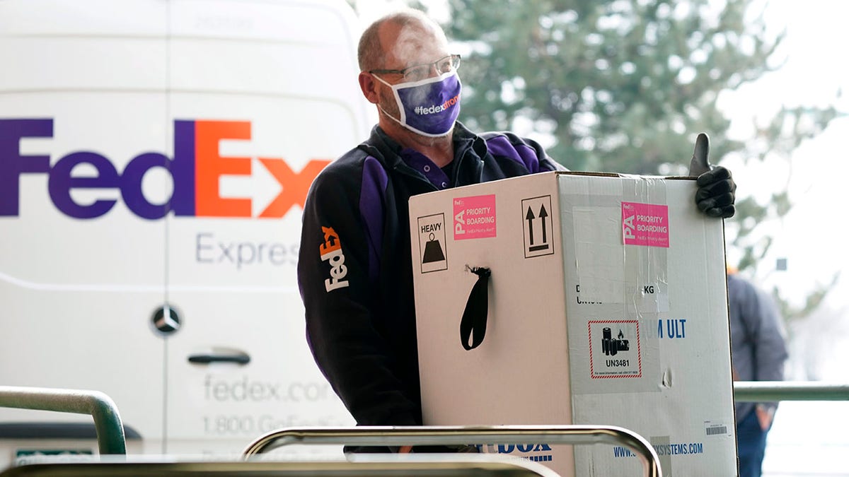 A FedEx driver carries a box to Colorado Gov. Jared Polis so he can sign for the delivery of the state's first shipment of COVID-19 vaccine at the Colorado Department of Public Health and Environment, early Monday, Dec. 14, 2020, in Denver. (AP Photo/David Zalubowski)