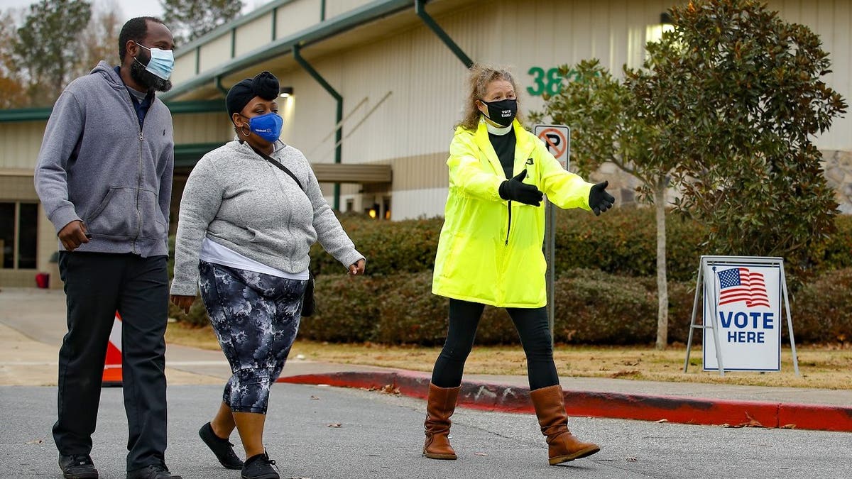 An Election Defender volunteer directs voters to an area where they can get free hand sanitizer and masks during early voting for the Senate runoff election at a recreation center Thursday, Dec. 17, 2020, in Powder Springs, Ga. (AP Photo/Todd Kirkland)