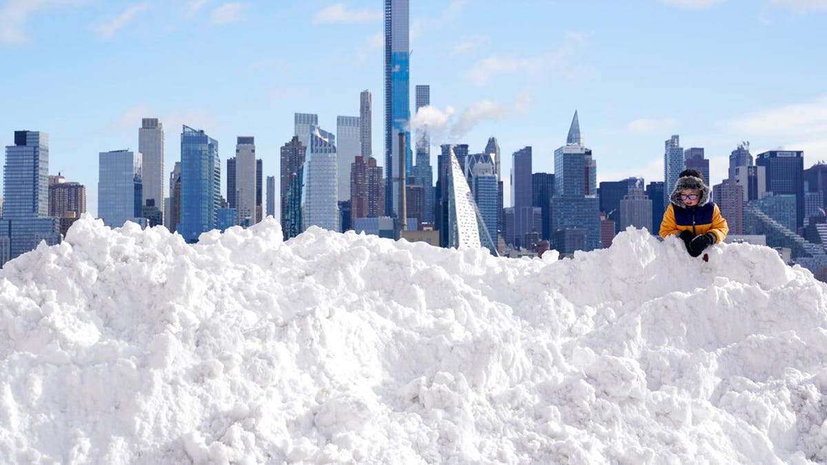 A boy plays on a mound of snow in front of the skyline of New York City in West New York, N.J., Thursday, Dec. 17, 2020. The first major snowstorm of the season left the Northeast blanketed in snow, setting records in some areas. (AP Photo/Seth Wenig)