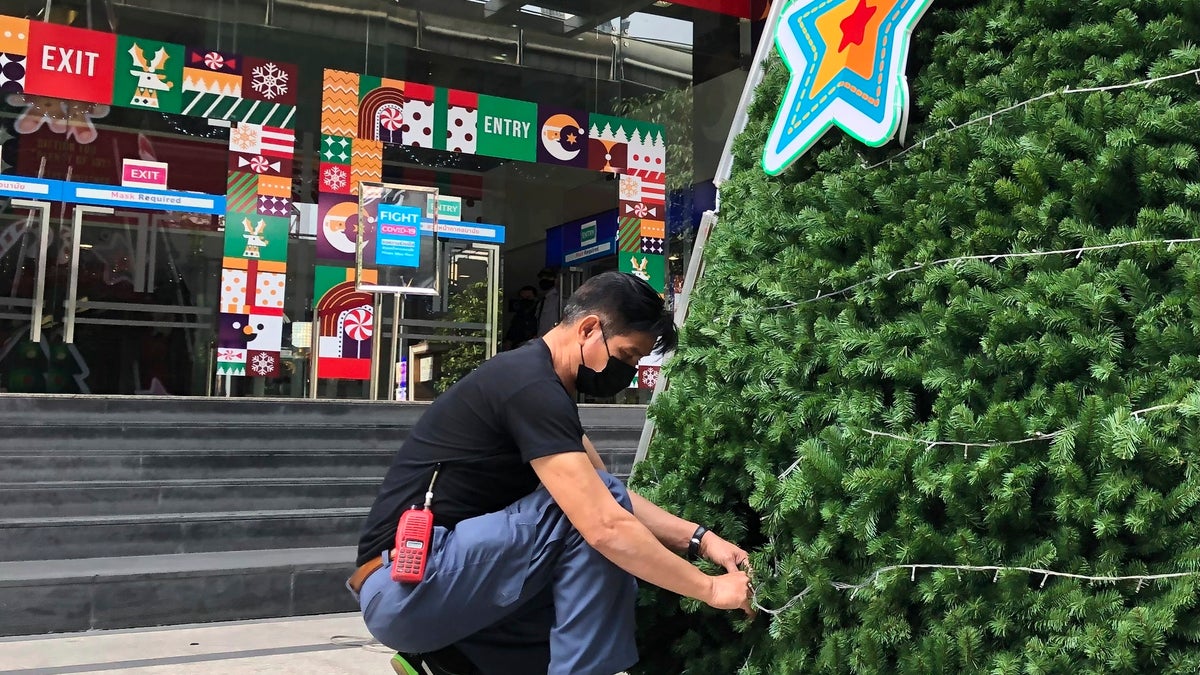 A worker wearing a face mask to help prevent the spread of coronavirus prepares an artificial Christmas tree outside a shopping mall that would normally be busy with foreign tourists in Bangkok on Wednesday, Dec. 23, 2020. Thailand has kept the coronavirus largely in check for most of the year but is facing a challenge from a large outbreak that threatens to undo months of efforts to contain the virus and hasten recovery of an ailing economy that relies heavily on tourism.(AP Photo/Adam Schreck)