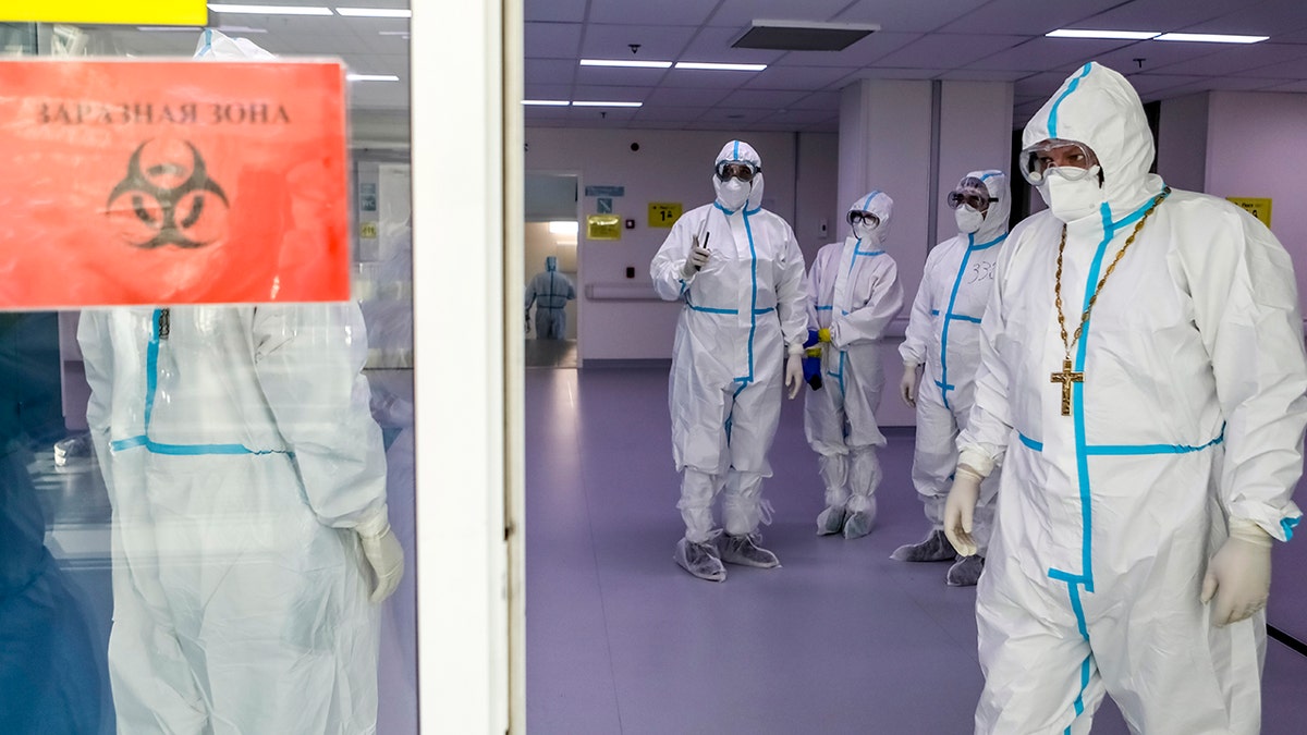 A Russian Orthodox Church priest, right, leaves a red zone after visiting patients suspected of having coronavirus at a hospital in Kommunarka, outside Moscow, Russia, Monday, Dec. 28, 2020. (Sophia Sandurskaya, Moscow News Agency photo via AP)