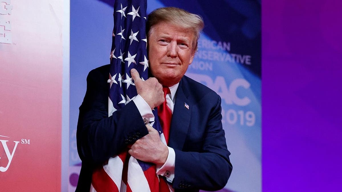 President Donald Trump hugs the American flag as he arrives to speak at the Conservative Political Action Conference, CPAC 2019, in Oxon Hill, Md., on March 2, 2019. Trump again hugged an American flag as he began his address to CPAC 2021. (AP Photo/Carolyn Kaster)
