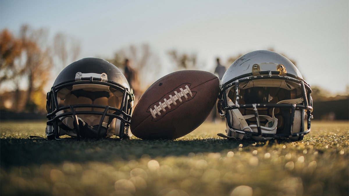 American football helmets and ball on the playing field, no people.