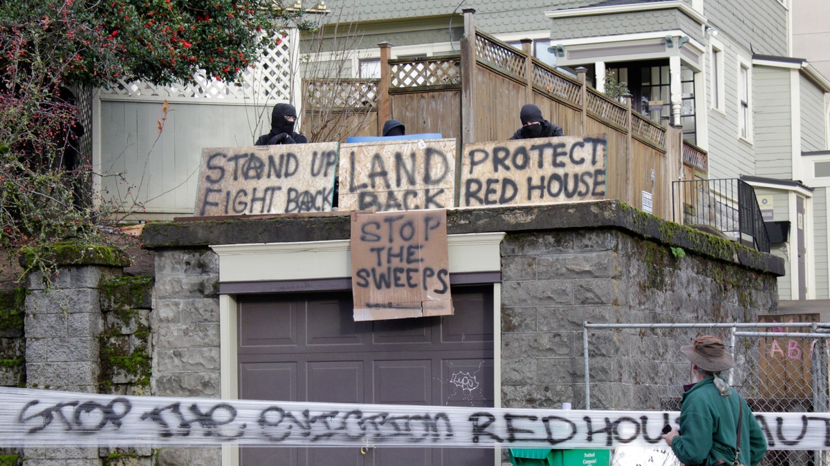 Masked protesters by an occupied home speak with a neighborhood resident opposed to their encampment and demonstration in Portland, Ore., on Wednesday, Dec. 9, 2020. Makeshift barricades erected by protesters are still up in Oregon's largest city a day after Portland police arrested about a dozen people in a clash over gentrification and the eviction of a family from a home. (AP Photo/Gillian Flaccus)